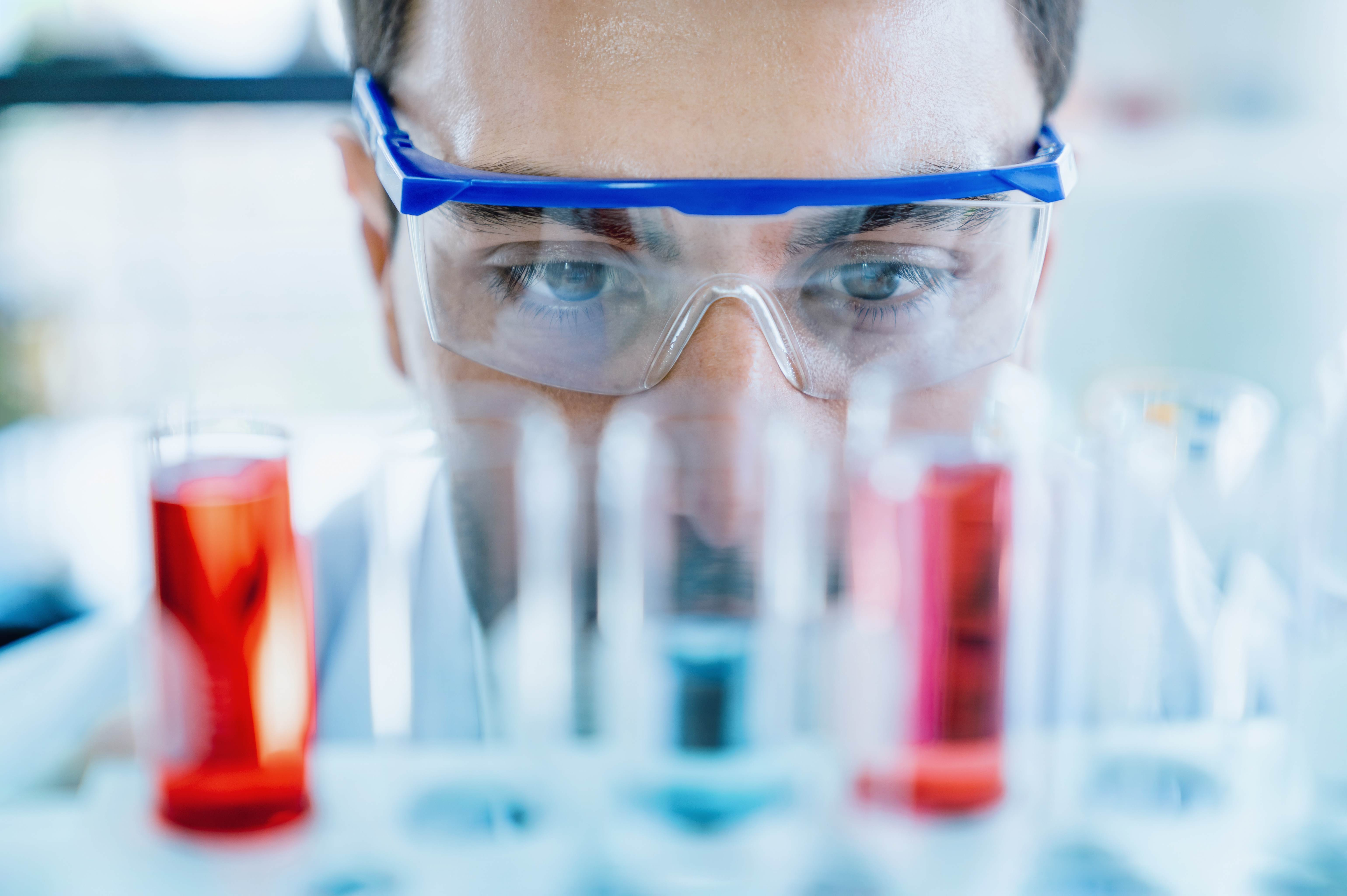 man in goggles looking at coloured test tubes